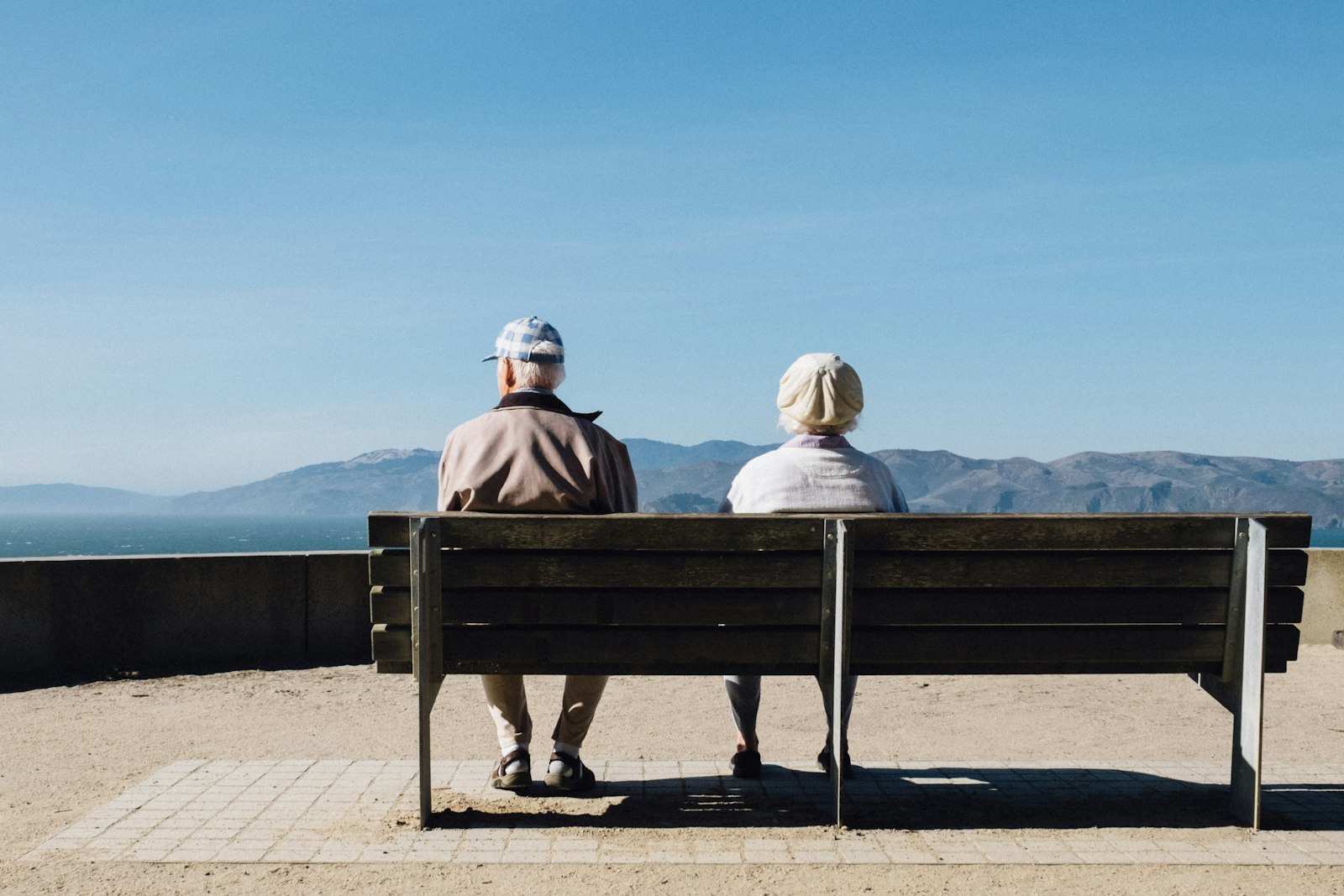Older couple sitting on a bench facing the sea
